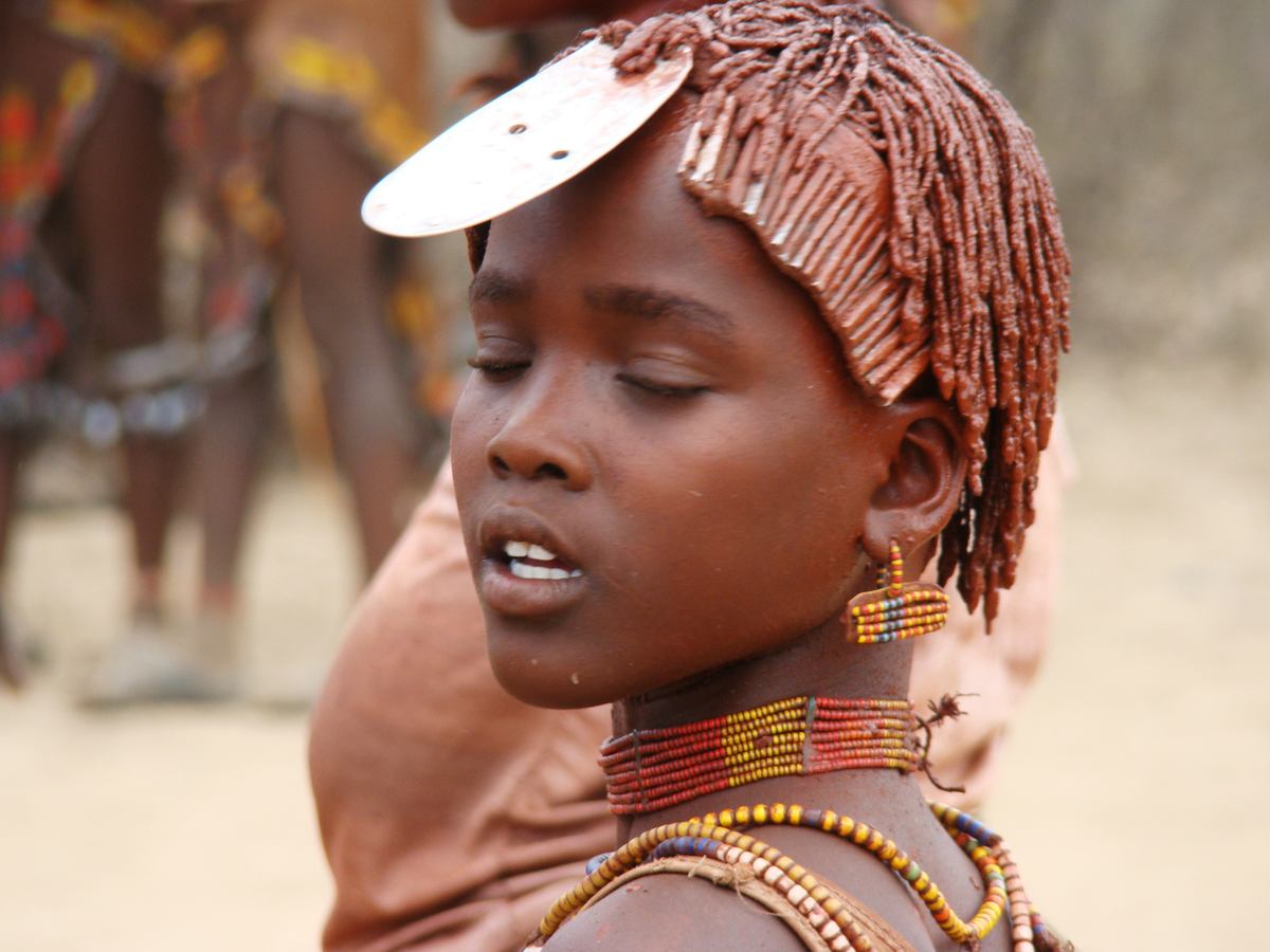 Jihozpadn Etiopie, dol Omo, Turmi: Dvka z kmene Hamar na slavnosti skkn pes bky. Stejn jako ostatn dvky na slavnosti m vlasy m naputn sms erven hlinky a tuku.